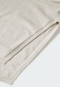 Gros plan d’un tissu tricoté beige clair avec un détail de bord plié, montrant une texture douce et des coutures fines.