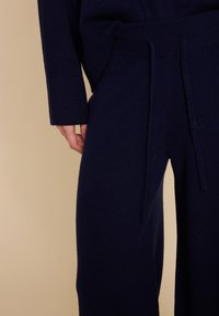 Marineblå strikkede loungewear-bukser med en myk tekstur. Har strikk i midjen og en avslappet passform, kombinert med en matchende strikket topp.