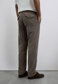 Pantalones de pana grises con un corte holgado, que presentan bolsillos en ángulo y un bolsillo trasero con botón, exhibidos en una persona de espaldas.