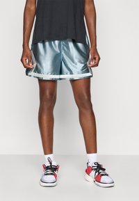 Lyseblå satinsportshorts med en glansfull finish, med lyse trim. Kombinert med hvite sneakers med røde detaljer og hvite sokker.