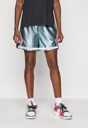 Lyseblå satin sportsshorts med en blank finish, der har lysfarvet kant. Kombineret med hvide sneakers med røde accenter og hvide sokker.