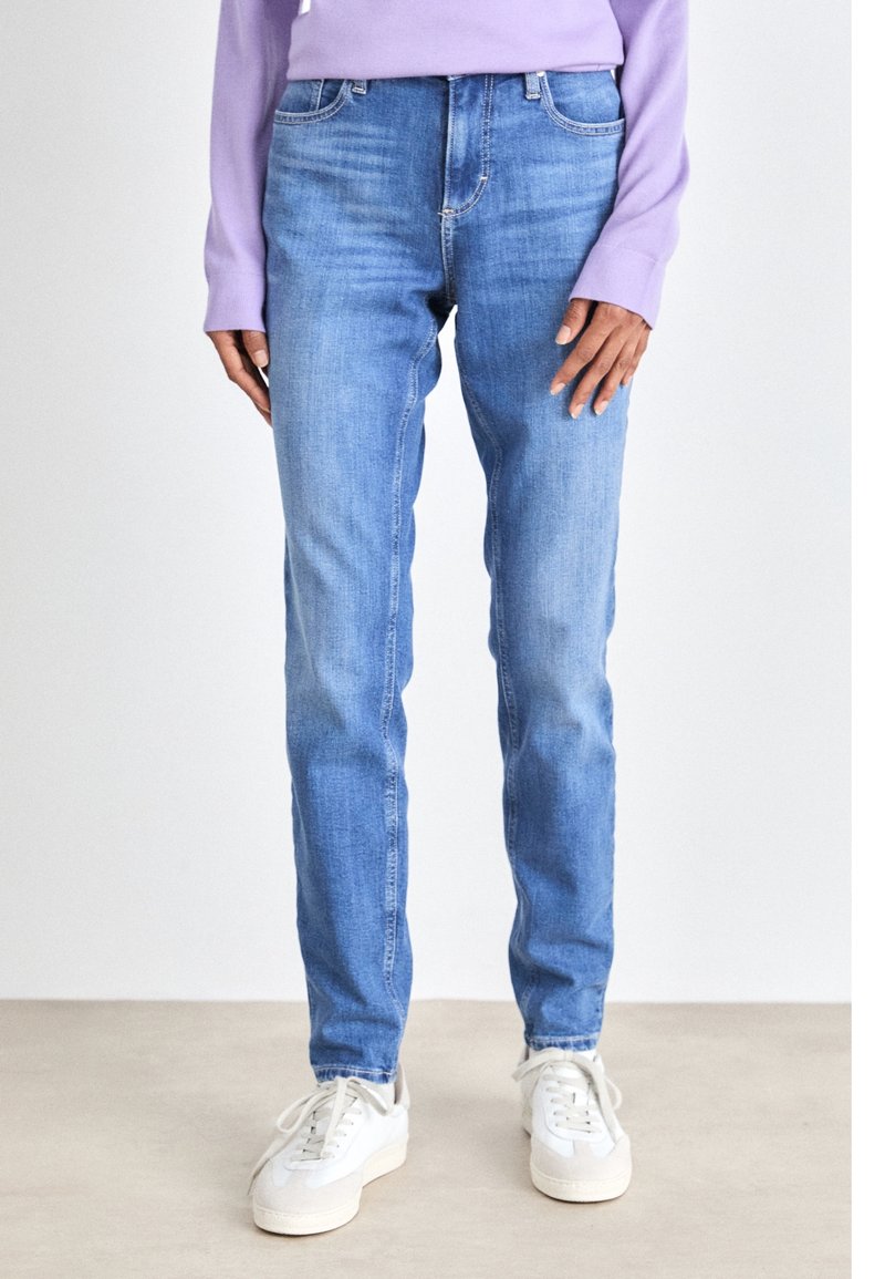 Jean denim bleu clair à coupe droite, avec cinq poches, une légère décoloration et des détails de couture discrets, associé à des baskets blanches.