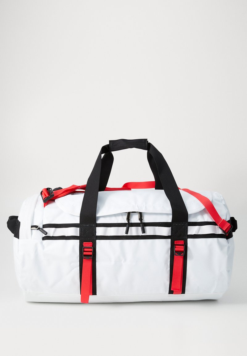 White duffle bag with black and red accents, features dual top handles, shoulder strap, and black horizontal stripes on the body.