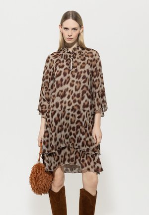 Leoprindkleid mit gestuftem Design, leichtem Stoff, Schlüsselloch-Ausschnitt, ausgestelltem Ärmeln und kombiniert mit einer strukturierten braunen Handtasche.