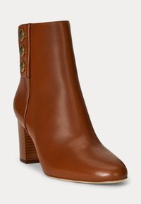 Botine din piele maro, cu vârful ascuțit și toc înălțat. Prezintă trei butoane decorative aurii pe lateral pentru un accent.