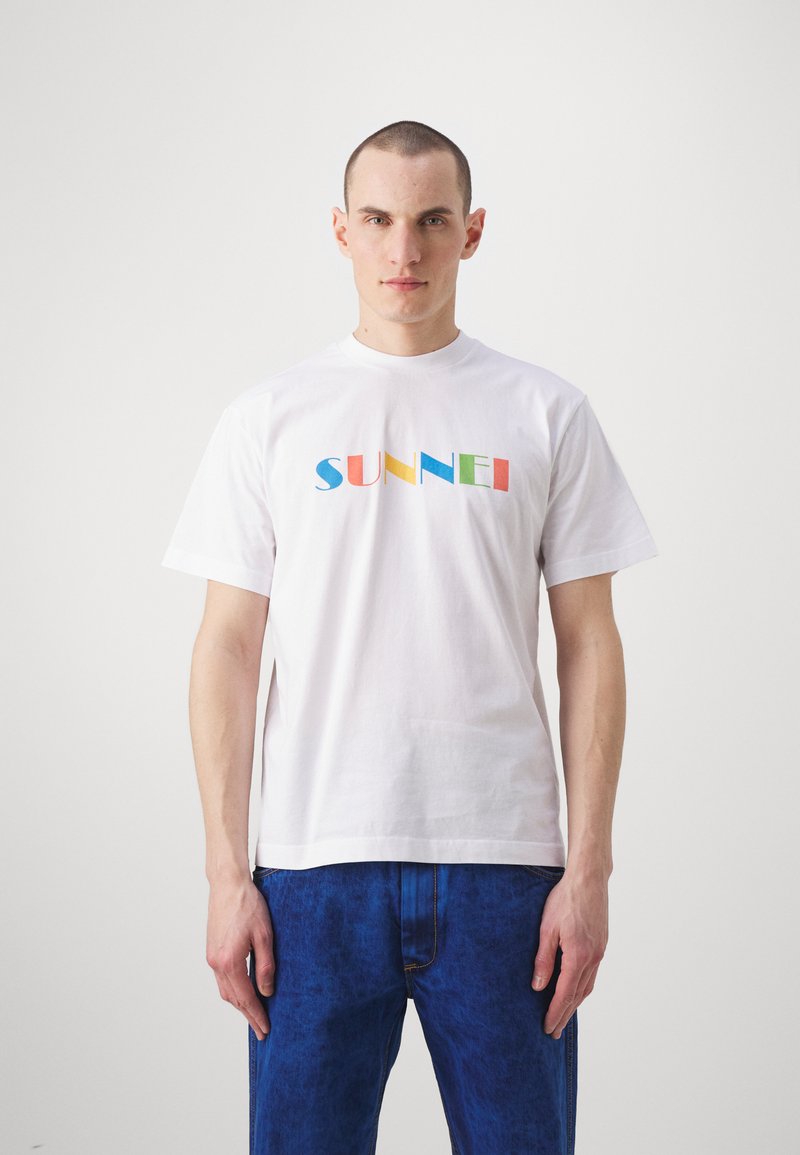 White cotton t-shirt featuring a multicolored "SUNNEI" logo in varying shapes. The shirt has short sleeves and a round neckline.