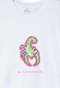 White t-shirt featuring a colorful graphic of a scorpion in green, purple, and pink, with the text "SATURDAYS" in pink below.