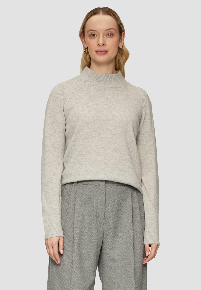 Hellgrauer Strickpullover mit hohem Kragen, langen Ärmeln und gerippten Bündchen. Kombiniert mit strukturierten grauen Hosen, die einen geschichteten Look kreieren.