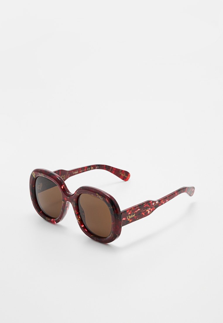 Rote Schildpatt-Sonnenbrille mit braunen Gläsern. Breite, abgerundete Rahmen mit glatter Textur und goldener Markenkennung an den inneren Bügeln.
