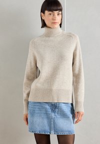 Beige coltrui van zachte breimateriaal met geribbelde manchetten en onderrand, gecombineerd met een lichtblauwe denim minirok.