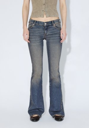 Vaqueros acampanados de mezclilla en azul medio con acabado desgastado, cinco bolsillos y herrajes plateados. Tela de algodón con textura suave.