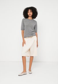 Hall halli lühikeste varrukatega top, mille juurde on kombineeritud beežid kõrge vöökohaga püksirihmad, millel on voldid, ning heledat halli seemisnahast libisemiskindlad kingad.