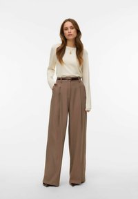 Haut beige à manches longues associé à un pantalon marron taille haute à jambes larges, avec une texture lisse et un détail de ceinture, sur fond blanc.