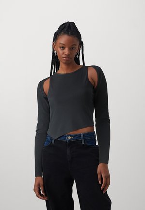 Black ribbed long-sleeve top with cut-out shoulders, curved hem, and a fitted design paired with high-waisted dark denim pants.