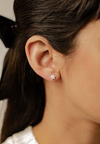 Orecchini a bottone d'argento con design floreale e molteplici piccole gemme trasparenti, indossati in un orecchio forato accanto a capelli lisci e scuri.