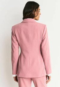 Roze getailleerd colbert met een gestructureerde pasvorm, een gladde textuur en een ingesneden revers. Achternaaddetails verbeteren de silhouet. Witte manchet komt tevoorschijn.