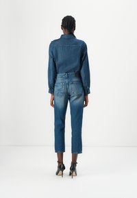Cămașă din denim cu manșete cu buton, purtată cu blugi scurți cu talie înaltă. Spălare închise, accente estompate pe genunchi, asortată cu tocuri înalte negre.