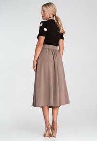 Czarny krótki top z różową aplikacją w kształcie kwiatu, zestawiony z długą, beżową spódnicą plisowaną. Przezroczyste, na wysokim obcasie buty dopełniają stylizację.