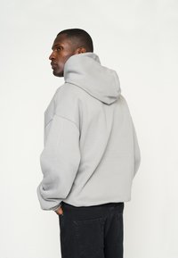 Grijze oversized hoodie met een grote capuchon, zachte textuur en verlaagde schouders, gecombineerd met donkere broek. Eenvoudig, casual ontwerp.