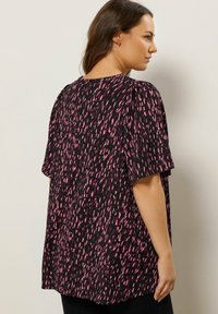 Sort bluse med løs pasform, der har et pink abstrakt mønster, korte ærmer og rund halsudskæring. Blødt stof med en let struktureret overflade.