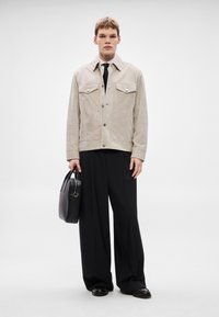 Bézs színű velúr dzseki két mellzsebbel, fekete nyakkendő, laza fekete nadrág és egy fekete táska, kerek fogantyúval.