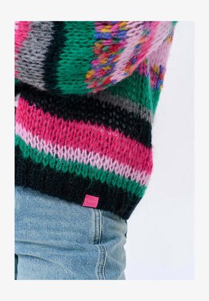 Kolorowy sweter na drutach z paskami w kolorach różowym, zielonym, czarnym i szarym, z małą różową metką przy krawędzi. Tekstura wygląda na miękką i przytulną.