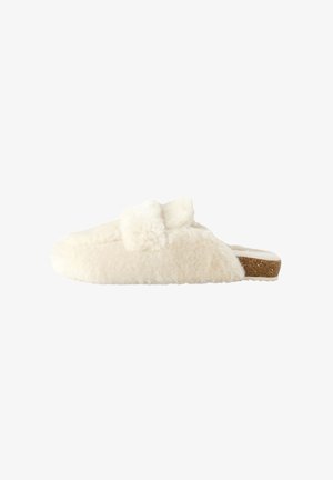 Kremowy pluszowy pantofel typu slip-on z korkową podeszwą i miękkim kokardkowym detalem na górze, pokazany z profilu na białym tle.