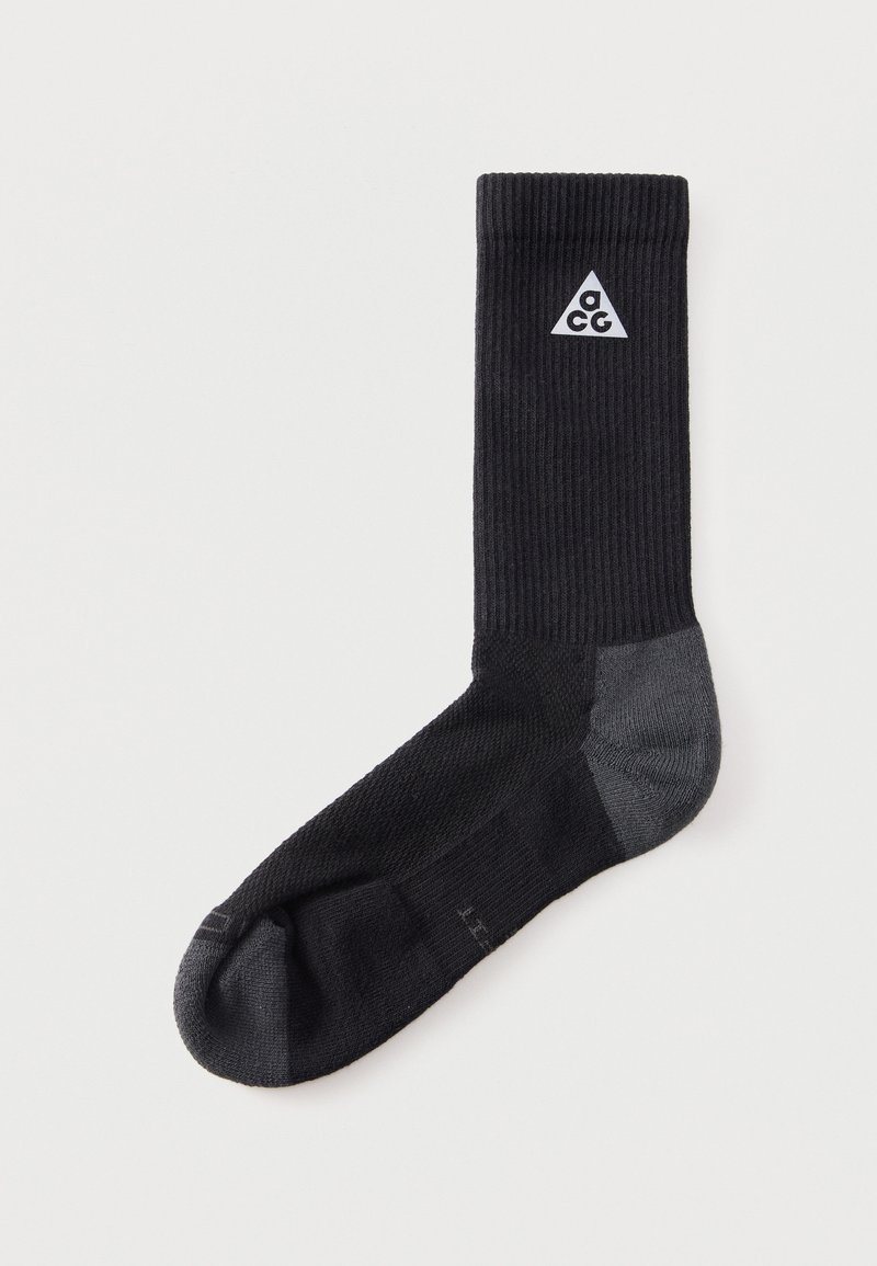Μαύρη αθλητική κάλτσα με γκρι φτέρνα και μύτη, με λευκό λογότυπο τριγώνου ACG κοντά στη πάνω μανσέτα σε απλό ανοιχτό φόντο.