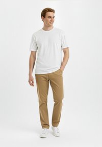 T-shirt in cotone bianco, chinos beige chiaro e sneakers bianche. La T-shirt ha un collo tondo; i chinos presentano una vestibilità regolare. Design semplice e casual.