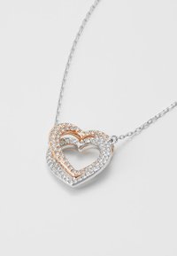 Naszyjnik z wisiorkiem w kształcie serca ze srebra i różowego złota z błyszczącymi, przezroczystymi kamieniami, z otwartym sercem w środku i cienkim łańcuszkiem.