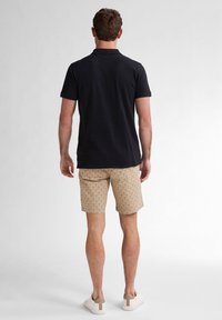 Polo shirt nera a maniche corte, pantaloni corti beige a fantasia con dettagli testurizzati e sneakers bianche con un accento marrone sul tallone.