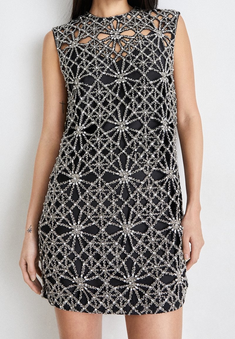 Robe noire sans manches avec des motifs floraux et géométriques argentés incrustés de perles couvrant le devant et les épaules.