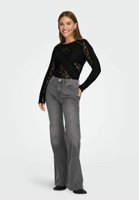 Black lace long-sleeve top featuring textured panels, paired with high-waisted, loose-fitting gray jeans and black ankle boots.