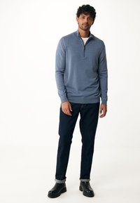 Ljusblå zip-halströja i mjukt material, kombinerad med mörka jeans och svarta ankelstövlar. Slät textur, avslappnad passform.