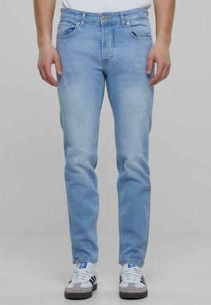 Light blue jeans made from denim, featuring a classic five-pocket design, slight fading, and a straight fit. Worn with white sneakers.