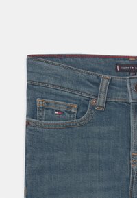 Jeans de mezclilla con un lavado azul oscuro, que presentan un pequeño bolsillo frontal, costuras clásicas y etiqueta de la marca en la cintura.