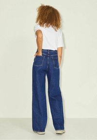 Högmidjade vida jeans i mörkblå denim, med två bakfickor och en avslappnad passform. Kombinerat med en vit t-shirt.