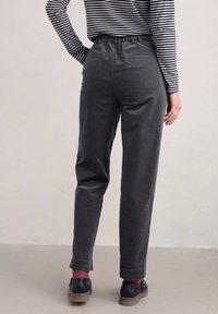 Pilki medvilniniai kelnes su elastingu liemeniu, siaurėjančiomis kojomis ir dviem galiniais kišenėmis. Modelis dėvi juostuotą marškinėlį ir tamsius batus su raudonomis kojinėmis.