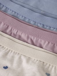 Pile de trois sous-vêtements en coton avec tailles élastiques en bleu, rose et crème, la paire crème présente un motif de petits cœurs bleus.
