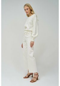 Maglione bianco lavorato a maglia con dettagli testurizzati nel colletto e jeans bianchi a gamba larga. Sandali con tacco marroni completano l'outfit.