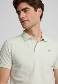 Polo verde chiaro in cotone, con colletto classico, maniche corte e un piccolo logo ricamato sulla parte sinistra del petto.