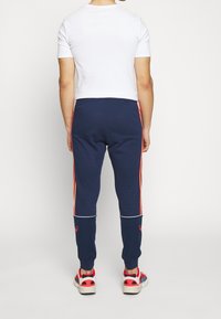 Námořnické joggery s červenými bočními pruhy, elastickým pasem a bílým lemováním. V kombinaci s přiléhavým bílým tričkem a sportovními teniskami.