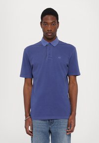 Blue polo shirt with a contrasting collar, three buttons at neck, short sleeves, and an embroidered logo on the left chest.