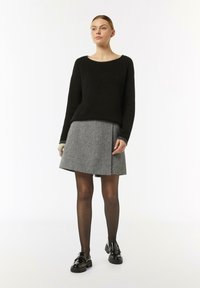 Schwarzer gerippter Pullover, grauer ausgestellter Rock mit strukturiertem Muster, durchsichtige schwarze Strumpfhosen und glänzende schwarze Loafers. Einfaches, modernes Design.