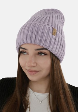 Young woman wearing a light purple ribbed knit beanie and a heart-shaped pendant necklace, with long brown hair and a soft smile.