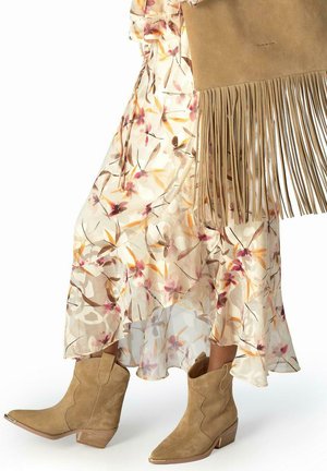 Botines de ante color canela con tacones apilados, combinados con una falda midi floral fluida y un bolso de ante con flecos color canela.