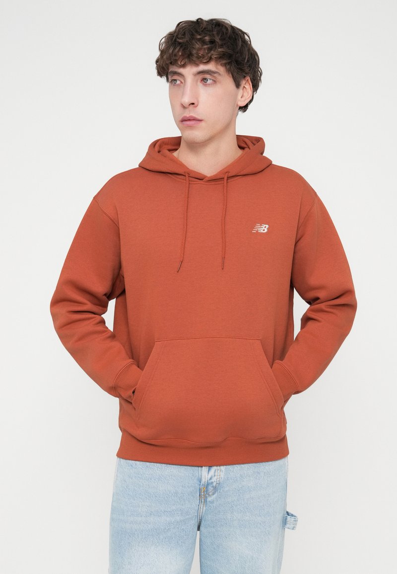 Kapuzensweatshirt in Rostfarbe aus weichem Stoff, mit Kordelzug, großer Kängurutasche vorne und kleinem Logo auf der Brust. Legerer Schnitt.