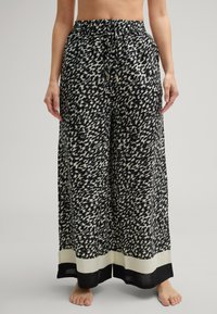 Spodnie szerokie w czarno-białym abstrakcyjnym wzorze, z elastycznym paskiem w talii i sznurkiem do regulacji, oraz kontrastującym czarnym wykończeniem na dole.