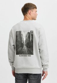 Sweatshirt gris avec un grand graphisme en noir et blanc d'une scène de rue au dos, avec le texte « BLEND SINCE 1993 » en dessous de l'image.