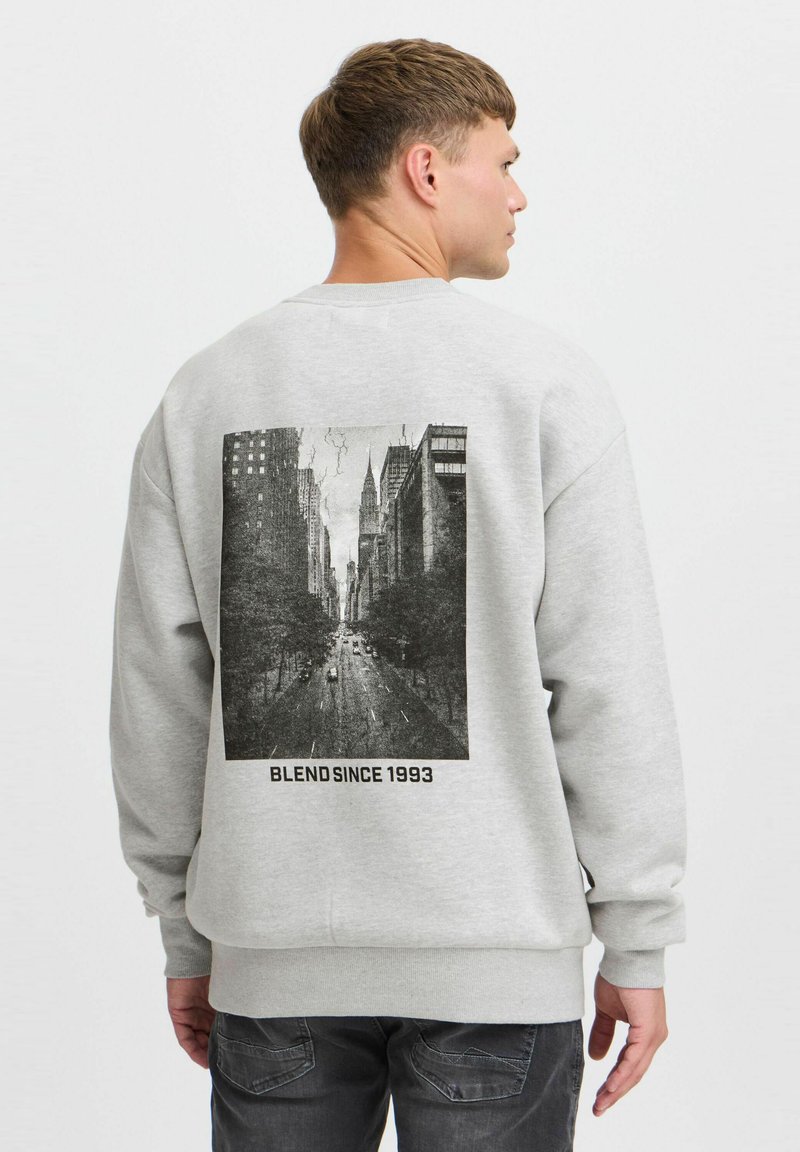 Sweatshirt gris avec un grand graphisme en noir et blanc d'une scène de rue au dos, avec le texte « BLEND SINCE 1993 » en dessous de l'image.